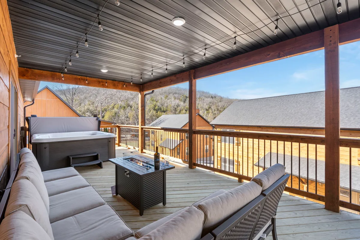 This exterior image showcases a welcoming deck area complete with a hot tub, comfortable outdoor seating, a coffee table, and a beautiful mountain view. The scene is set during a tranquil time, likely at sunset, emphasizing the relaxing ambiance and inviting environment for unwinding outdoors.