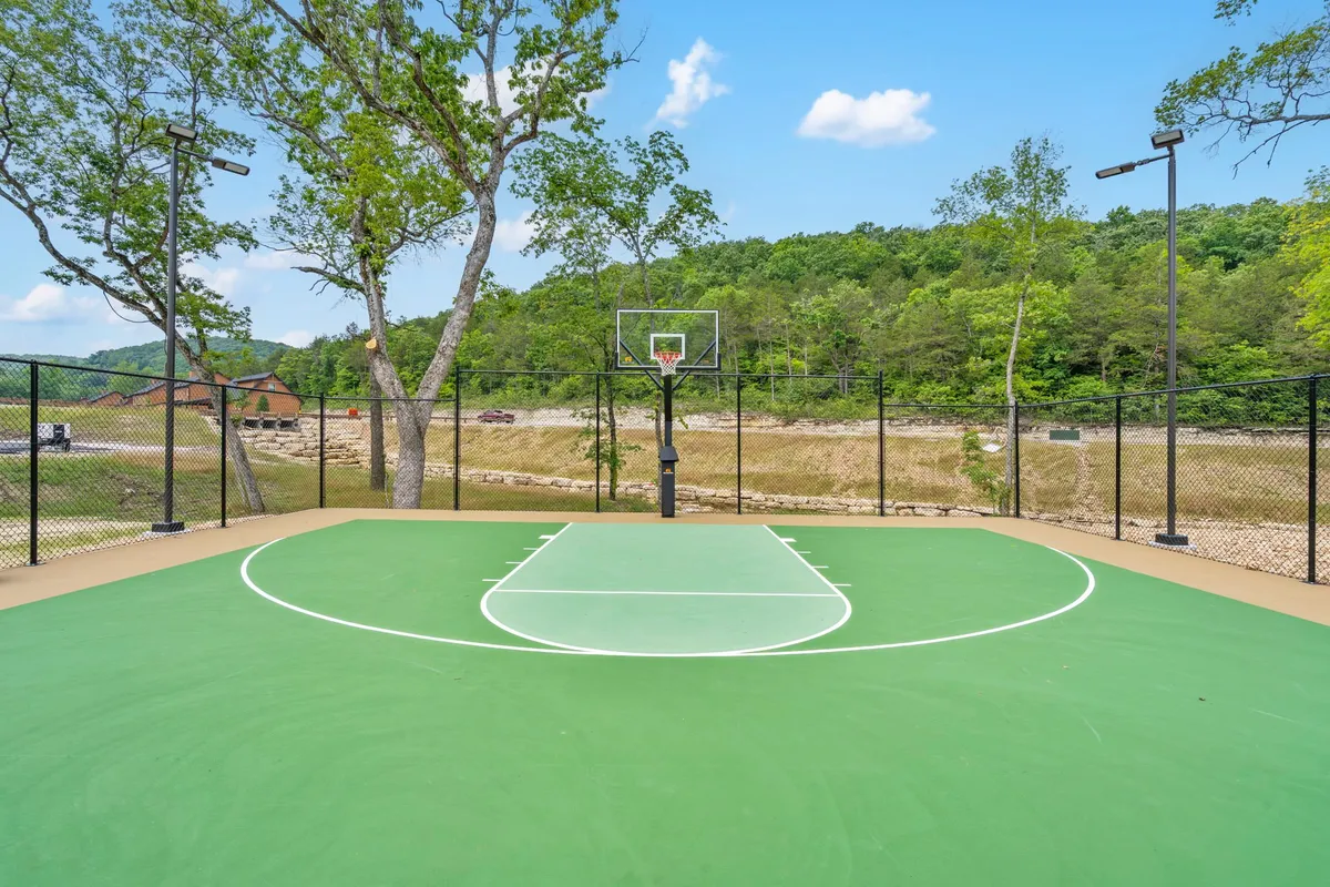 A scenic basketball court sits amidst tall trees with mountains visible in the distance. The court invites friendly games and energetic play, serving as a hub for community bonding and outdoor recreation.