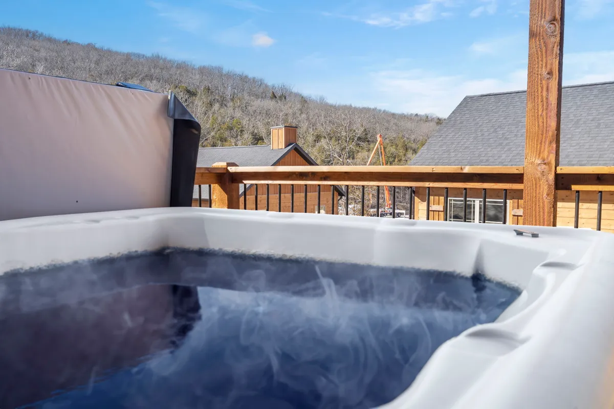 This exterior shot centers on a hot tub nestled against the deck railing, with a panoramic mountain view stretching beyond. The scene evokes the peaceful experience of soaking outside while being immersed in nature.