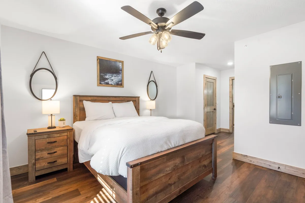 A calm and peaceful bedroom scene featuring a bed with soft bedding, complemented by nightstands, mirrors, and tasteful artwork. The space is brightened by natural light streaming in, evoking a sense of tranquility and restfulness.