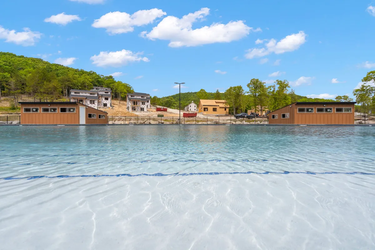 A calm water surface reflects the sky and surrounding wooded hills, with wooden structures dotting the shoreline. The setting suggests opportunities for fishing, boating, or simply relaxing by the water.