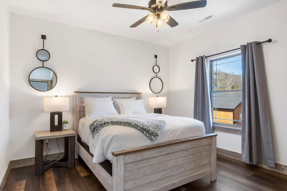 A cozy bedroom scene with a comfortable bed, wall mirrors, nightstands, and curtains. The room exudes calm, with natural light filtering in to highlight the inviting atmosphere and plush furnishings.