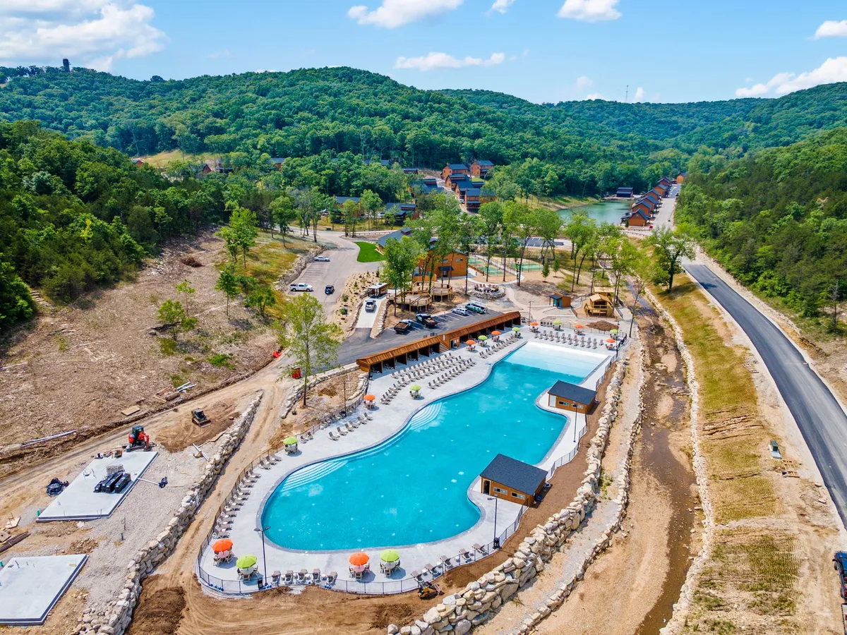 An outdoor pool glistens under the sun, surrounded by lush greenery, poolside lounge chairs, and wooden cabanas. The relaxed setting is ideal for sunbathing, swimming, and hosting outdoor family gatherings or community pool parties, capturing the spirit of summer recreation.