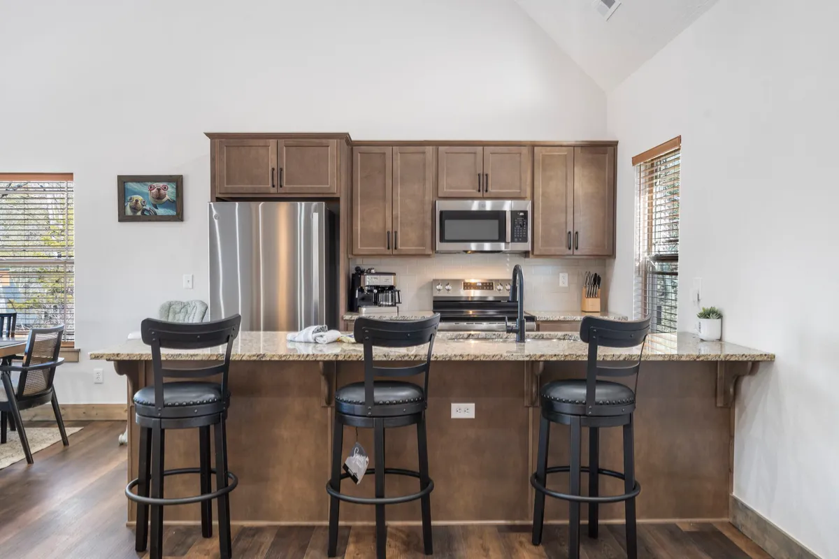 This image focuses on a modern kitchen with a prominent kitchen island, bar stools, stylish cabinetry, and stainless steel appliances—perfect for group meals, s’mores, or late-night snacks.