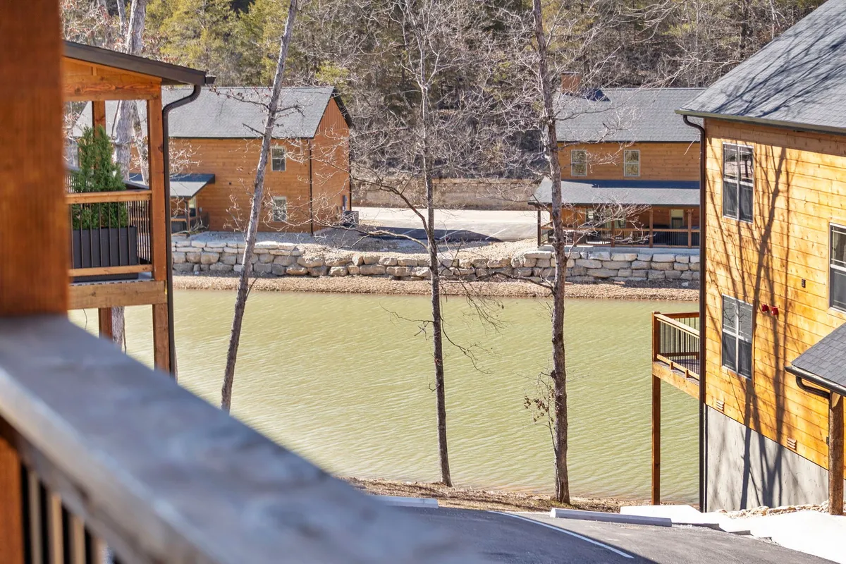 A scenic image featuring a serene lake (pond), wooden cabins along the shoreline, lush trees, and a soft sunset glow. The calm water and natural setting evoke a sense of tranquility and connection to the outdoors.