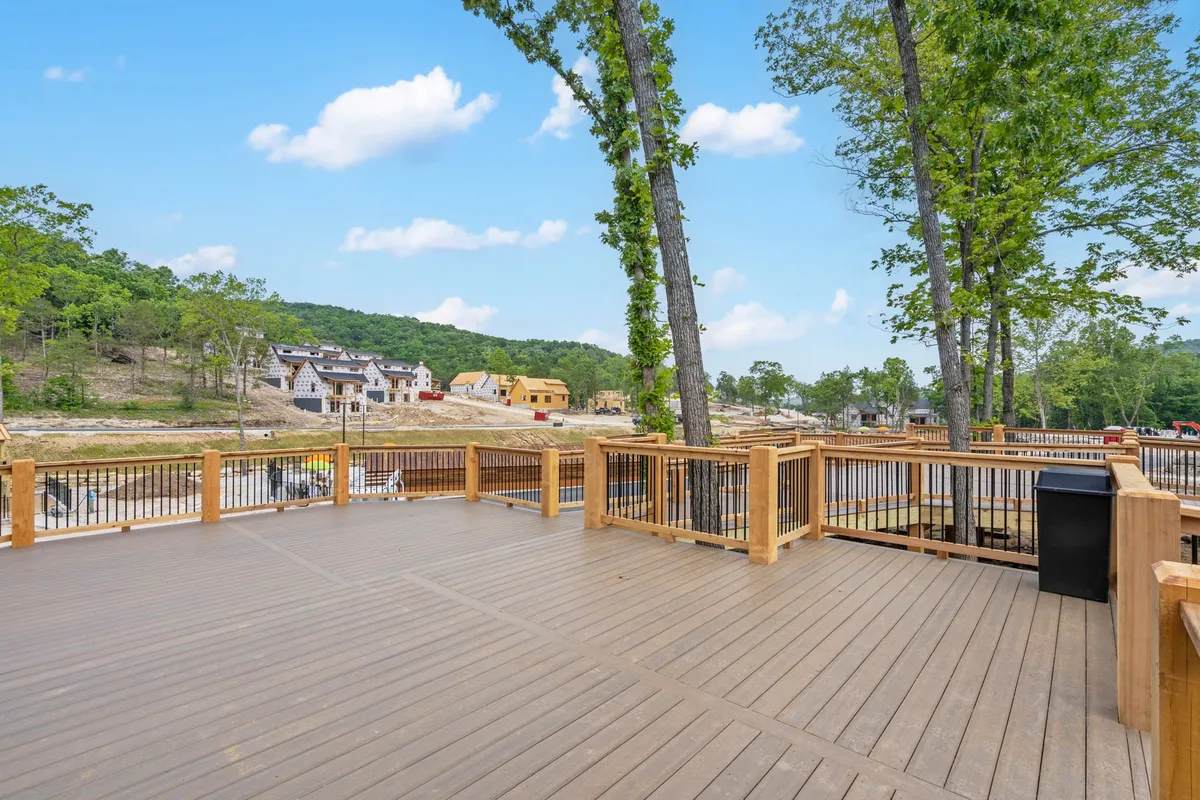 A spacious wooden deck with outdoor seating, set among trees with distant houses visible, offering a tranquil setting for morning coffee chats or group relaxation.