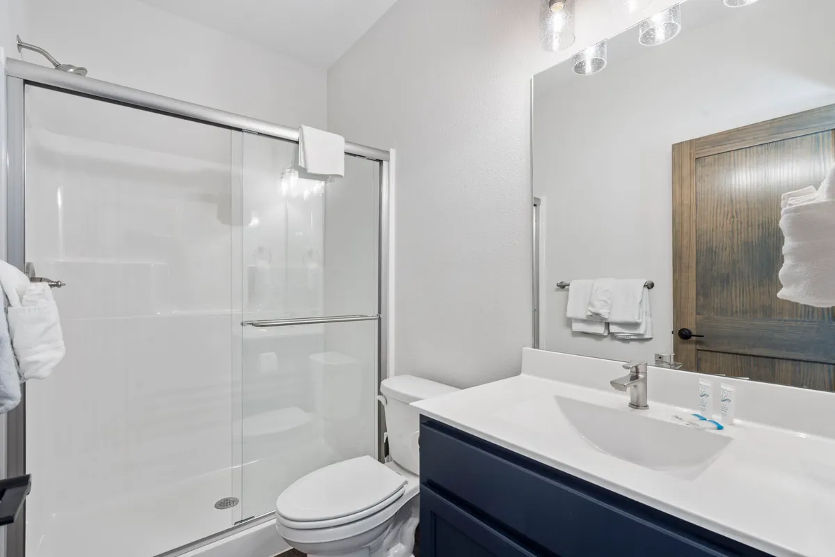 A modern ensuite bathroom featuring a glass shower, blue cabinetry, a sleek modern faucet, and a spacious mirror. The space feels fresh and serene, ideal for relaxing self-care routines.